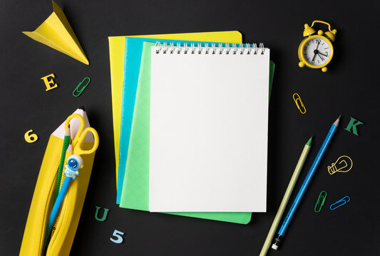 Creative school background with empty notebook surrounded by yellow and blue stationery on a blackboard. Concept of back to school or learning.