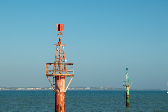 Red and green maritime lateral navigation beacons marking coastal channel in sea