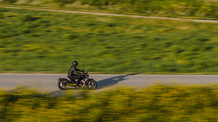 The drone-captured shot, using panning, shows a motorcycle riding along a winding asphalt road. The...