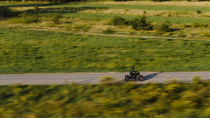 The drone-captured shot, using panning, shows a motorcycle riding along a winding asphalt road. The background blurs with motion, emphasizing the bike’s speed and direction, while the sharp focus stay