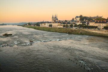 Water surges toward the viewer on a wide river beneath a pastel dawn. Amboise, France, with its cathedral spires and old buildings, basks in the soft morning light along the shore