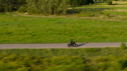The drone-captured shot, using panning, shows a motorcycle riding along a winding asphalt road. The...