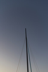 A vertical low-angle shot captures the mast of a sailboat and its rigging lines reaching into a...