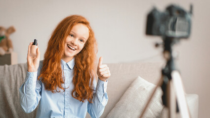 Beauty Advice And Blog. Smiling female teen doing makeup, recording cosmetics product review, showing her foundation for young skin to camera on tripod. Girl filming video, showing thumbs up