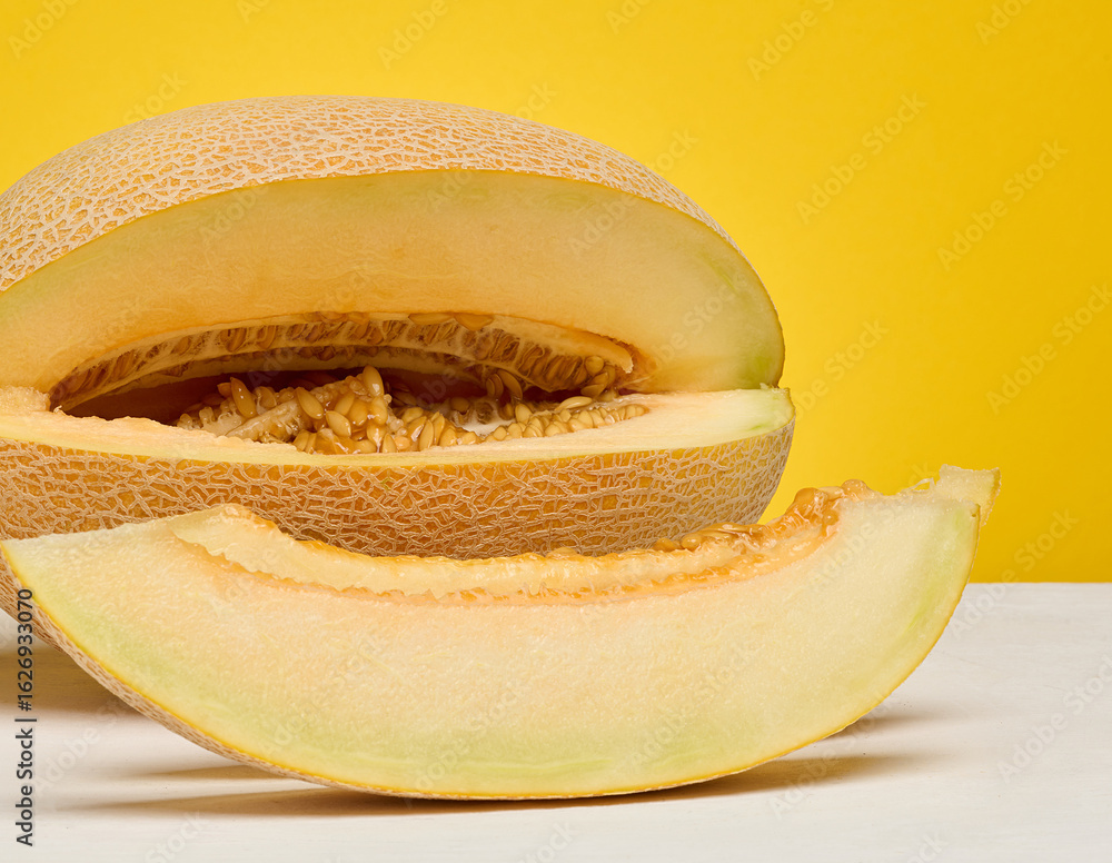 Poster half of a cantaloupe melon and a single slice placed on a white surface. yellow background.