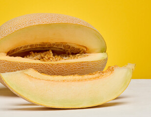 Half of a cantaloupe melon and a single slice placed on a white surface. Yellow background.