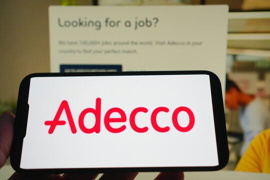 Roosendaal, The Netherlands - August 03, 2025: A mobile phone displaying the company logo of Adecco, with the company website in the background.