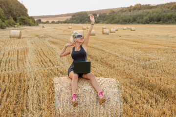 Beautiful blonde with laptop in a field with haystacks. Fashion. Photo model. Posing