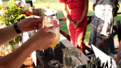 Close-up of bartender decorating yellow cocktail with flower as women watch at outdoor evening bar