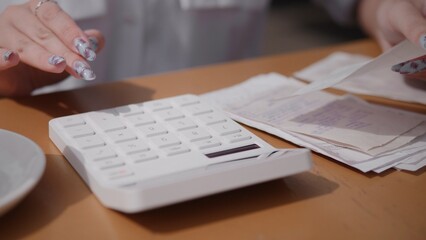 A closeup view of hands skillfully using a calculator, with cash, documents, and files scattered on...