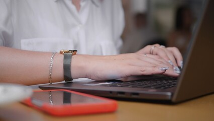 A person types on a laptop with a smartphone nearby, illustrating modern work and productivity in...