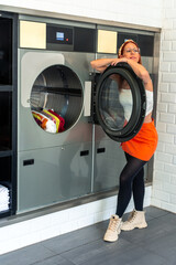 Woman waiting for laundry in laundromat with clothes dryer and washing machine