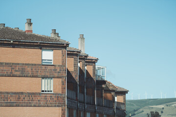 Row of red brick residential buildings with chimneys under clear blue sky, captured in telephoto...