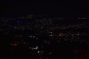 Shillong city at night, illuminated by countless lights against a dark sky, showcasing a bustling urban landscape.