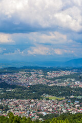 Obraz premium Shillong city nestled amidst hills and lush greenery, showcasing a panoramic view under a cloudy sky.