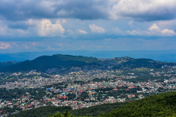 Shillong city nestled amidst hills and lush greenery, showcasing a panoramic view under a cloudy sky.