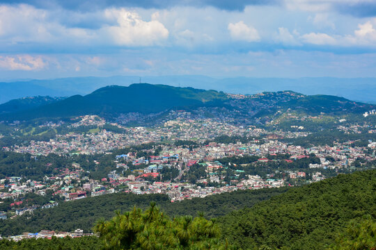 Shillong city nestled amidst hills and lush greenery, showcasing a panoramic view under a cloudy sky.