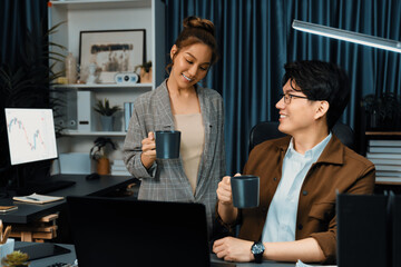 Sales managers discussing while drinking coffee cup together at over late night at home office, concept of modern working place with business report at breaking time with coworker at desk. Infobahn.