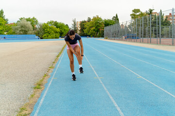 Young woman runner feeling a strong pain in her leg while training on a blue running track