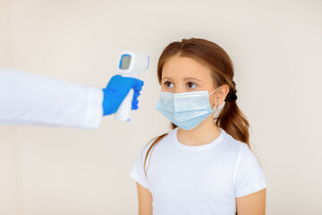Little girl in face mask having her temperature checked by electronic thermometer while waiting for...