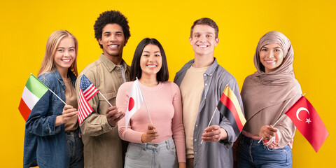 Friends, team, international language course and modern education. Happy young multiracial students holding flags of their countries isolated on orange background, copy space, studio shot
