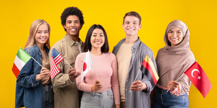 Friends, team, international language course and modern education. Happy young multiracial students holding flags of their countries isolated on orange background, copy space, studio shot - Powered by Adobe