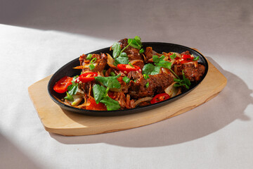 Spicy Korean pork ribs with red chili peppers, kimchi, onion and fresh greens served on a hot black skillet in natural light