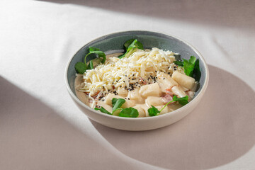 Soft Korean rice cakes in creamy cheese sauce with sesame seeds and fresh greens served in a...
