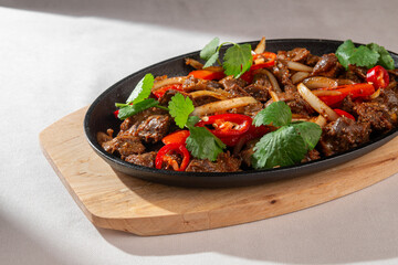 Spicy Korean pork ribs with red chili peppers, kimchi, onion and fresh greens served on a hot black skillet in natural light