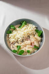 Soft Korean rice cakes in creamy cheese sauce with sesame seeds and fresh greens served in a...