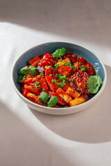 Korean rice cakes cooked in spicy gochujang sauce with vegetables, sesame seeds and fresh herbs served in ceramic bowl under natural daylight