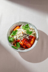 Spicy Korean rice cakes in gochujang sauce topped with shredded cheese, sesame seeds and fresh greens, served in ceramic bowl under natural light