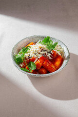 Spicy Korean rice cakes in gochujang sauce topped with shredded cheese, sesame seeds and fresh greens, served in ceramic bowl under natural light