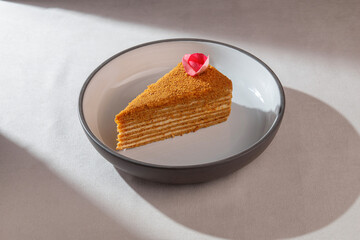 Traditional honey layered cake with soft cream and golden crumbs served with an edible flower on ceramic plate under soft natural light