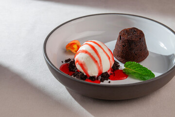 Warm chocolate fondant served with vanilla ice cream, strawberry syrup, mint leaf and edible flower on a ceramic plate in soft natural daylight