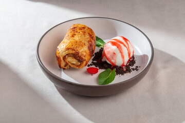 An appetizing golden-brown apple strudel beautifully paired with a scoop of creamy vanilla ice cream drizzled with berry sauce and fresh mint leaves