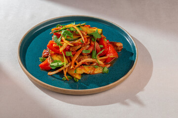 A colorful and appetizing Asian-style warm salad featuring tender pork, vibrant bell peppers, fresh cucumbers, and fragrant cilantro on a dark teal plate