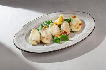 Appetizing baked mussels in their shells, topped with melted creamy cheese, garnished with fresh herbs and a bright lemon wedge, served on an oval plate