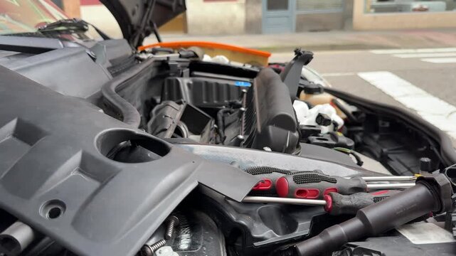 Close up video showing engine components and tools under open car hood during repair 