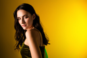 Portrait of a glamorous brunette wearing an elegant green dress against a vibrant yellow background