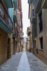 A charming narrow street winds through a colorful European town, bathed in sunlight.