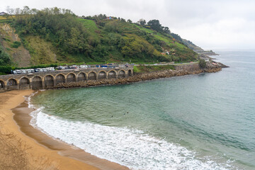 Picturesque coastal scene featuring a beach, arched viaduct, and a lush green hillside on an...