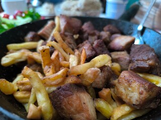 Traditional fried potatoes with pork and mushrooms close-up in a frying pan.