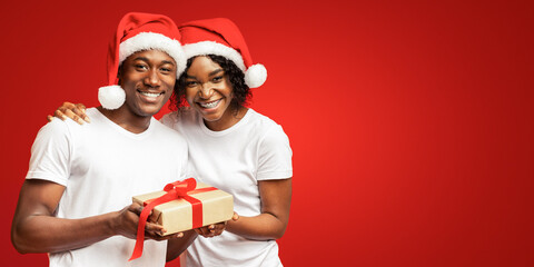 Happy black man and woman celebrating Christmas together, orange studio background, empty space....