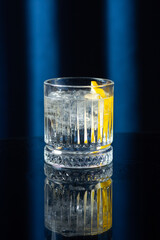 A close-up of a clear cocktail with ice and a lemon twist in a crystal glass, placed on a dark...