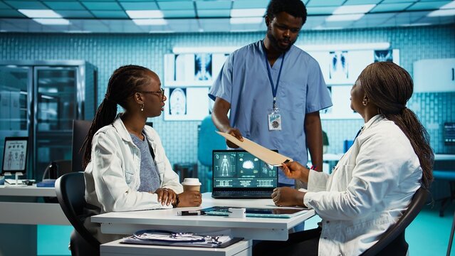 Black medical staff and patient discussing diagnostic feedback and records, emphasizing expertise and data driven decision making. Young adult listens to professional advice for wellness. Camera B.