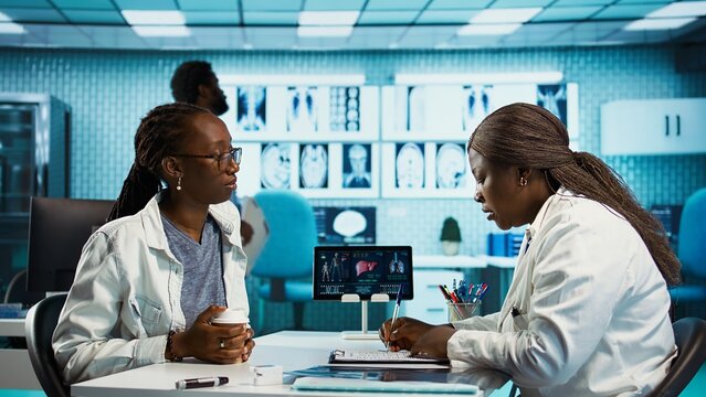 Female general practitioner examining medical data with a patient, fostering interaction and trust during expert consultation focused on wellness. African american girl asks for advice. Camera B.