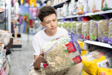 Interested teenage boy choosing safe straw bedding for cage of small pets in store, carefully...