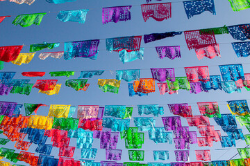 Looking up at a large group of colorful latin flags hanging against a blue sky