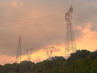 Line of Transmission Towers on a Forested Hill at Sunset
